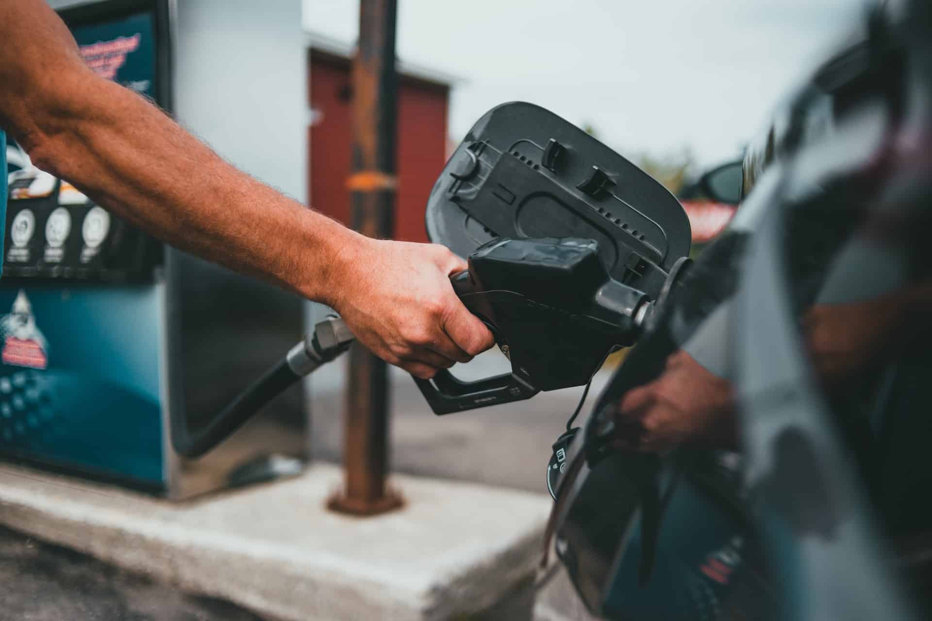 a person's arm holds the nozzle of a gas pump as it is filling up the tank of a car