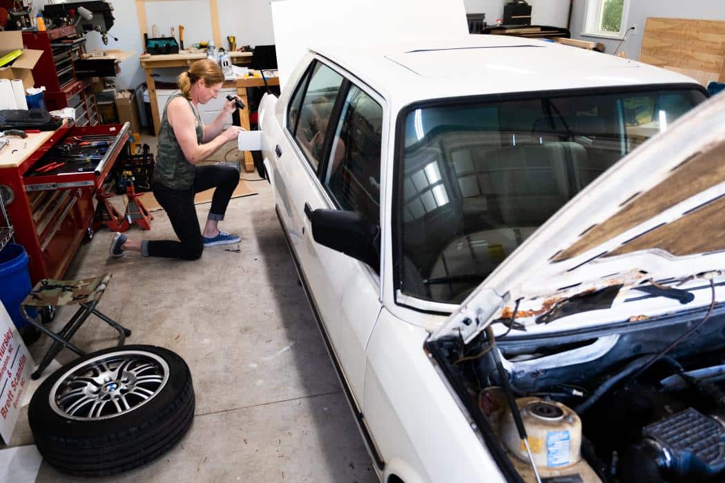 anna hursley works on her 1988 white bmw in the back of her garage